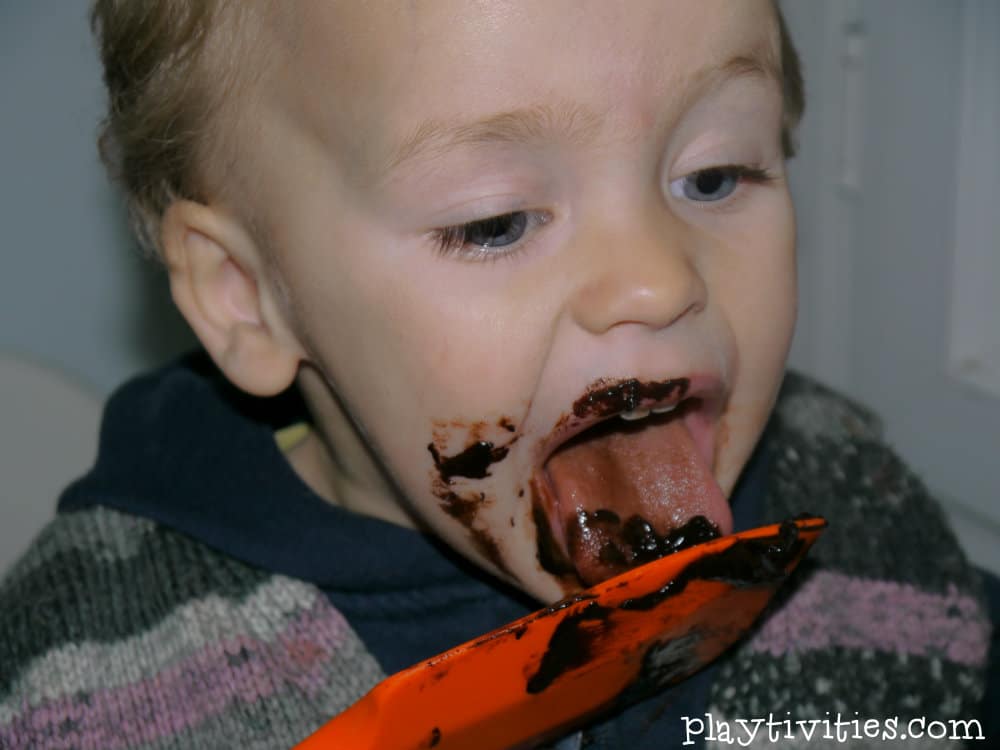 Young boy licking a spatula with a chocolate.