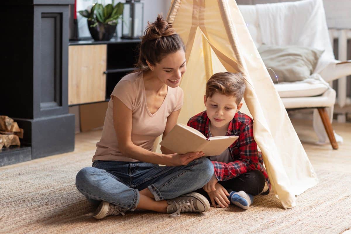 Young mother showing her son a book in a living room near a teepee.