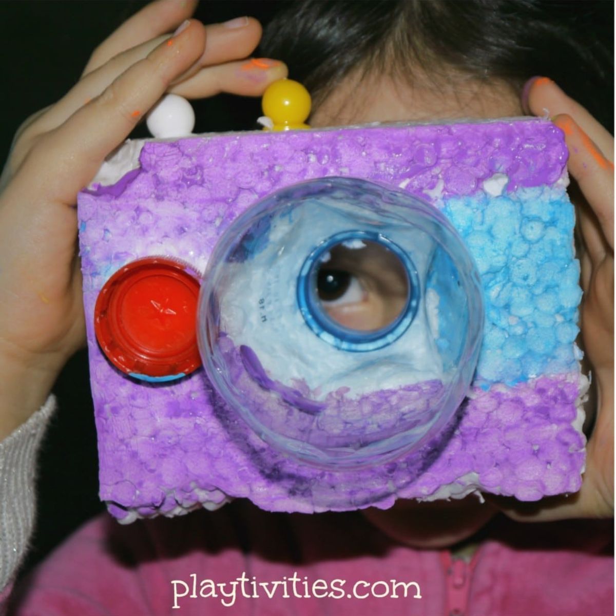 Young girl playing with a styrofoam toy camera.