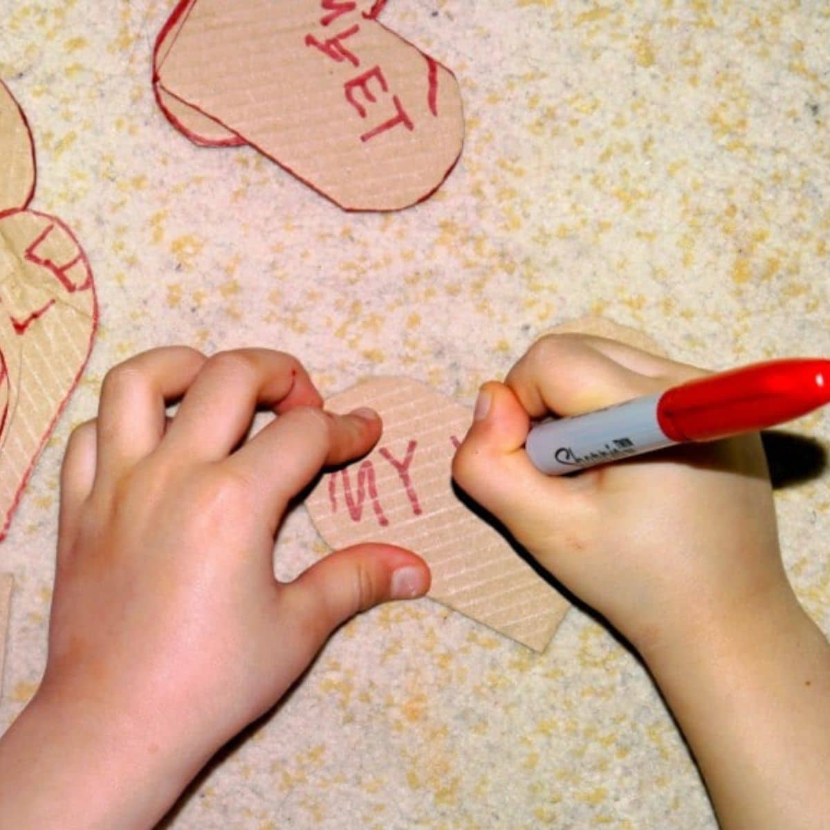 Kid hands with a red marker writing on carboard hearts.