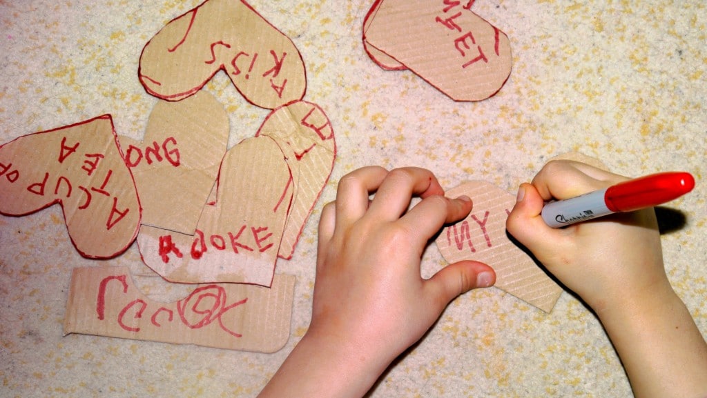 Kid with a red marker writing on a cardbord hearts.