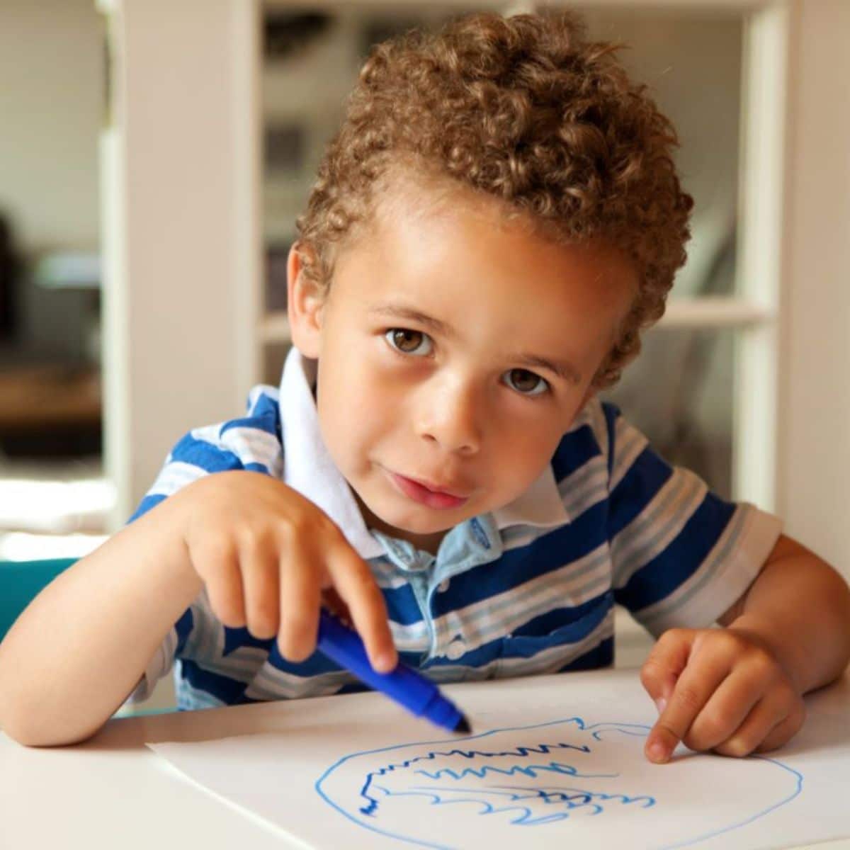 Toddler with a blue marker drawing on a paper sheet.