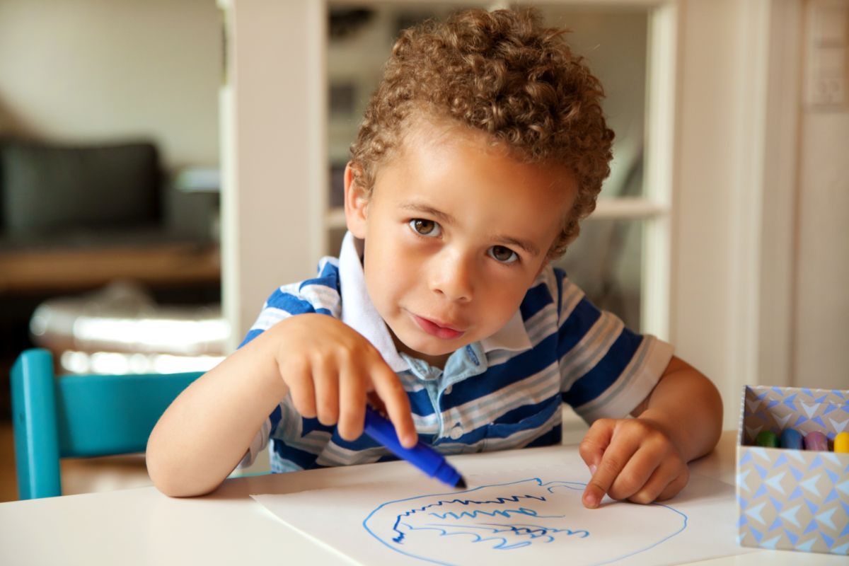 Toddler drawing with a blue marker on a paper sheet.