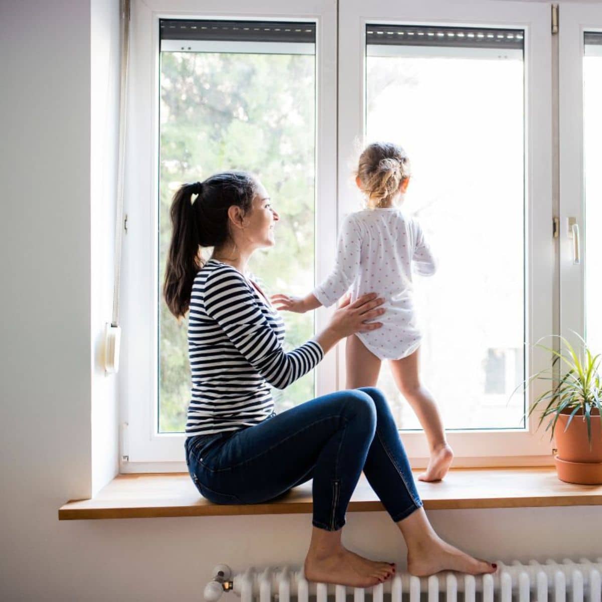 Young woman playing with her daughter near a window.