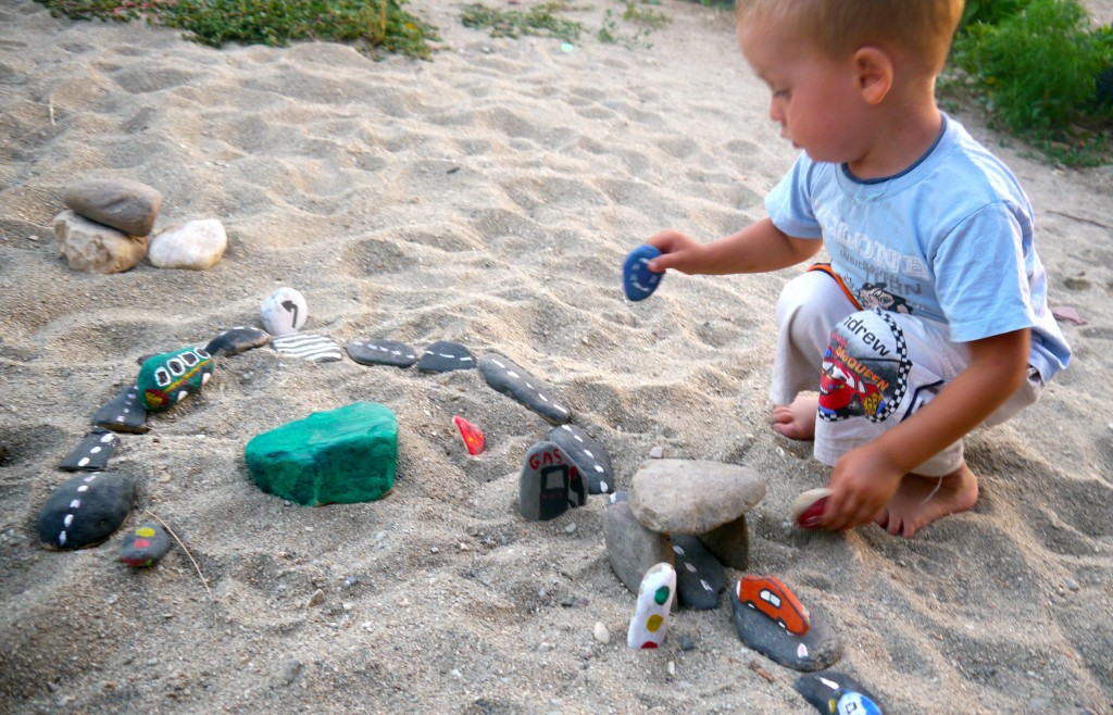 Young boy playing with a DIY Car Rock track. on a beach.
