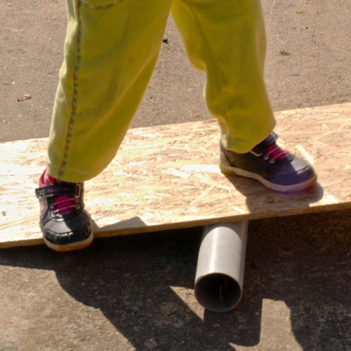 Kid holding a balance on a wooden board on a plastic pipe.