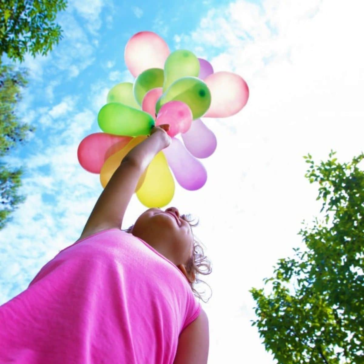 Young girl in pink dress holding balloons.