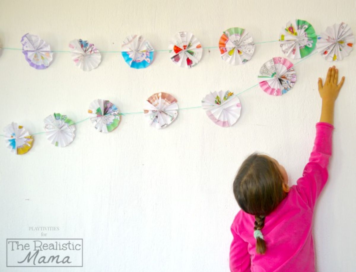 Young girl reaching paper garlands on a wall.
