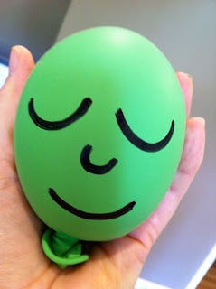 Hand holding a green ballon with a drawed face.