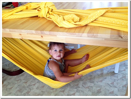 Toddler sitting under table in a yellow blanket.