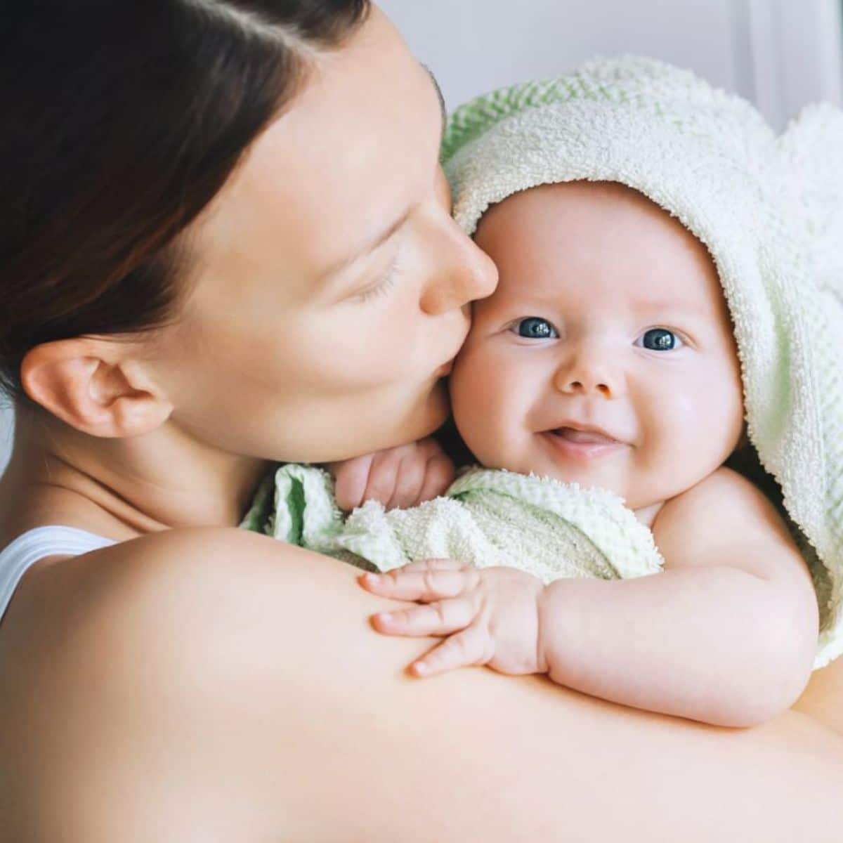 Young mother hugging and kissing her baby wrapped in a towel.