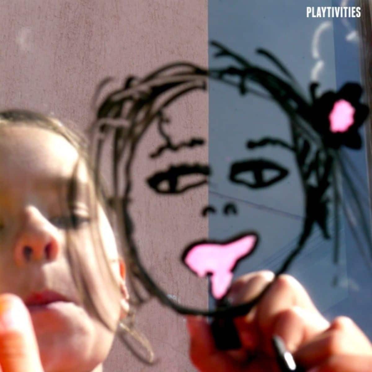 Young girl drawing a face on a mirror.