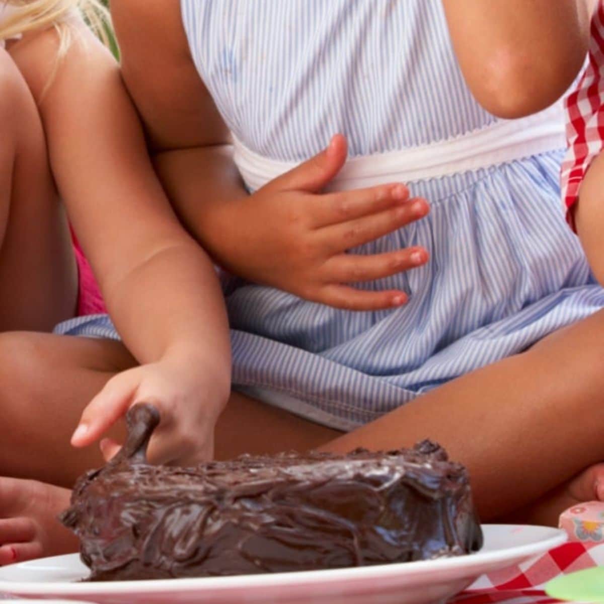 Young kids touching a cake on a plate.
