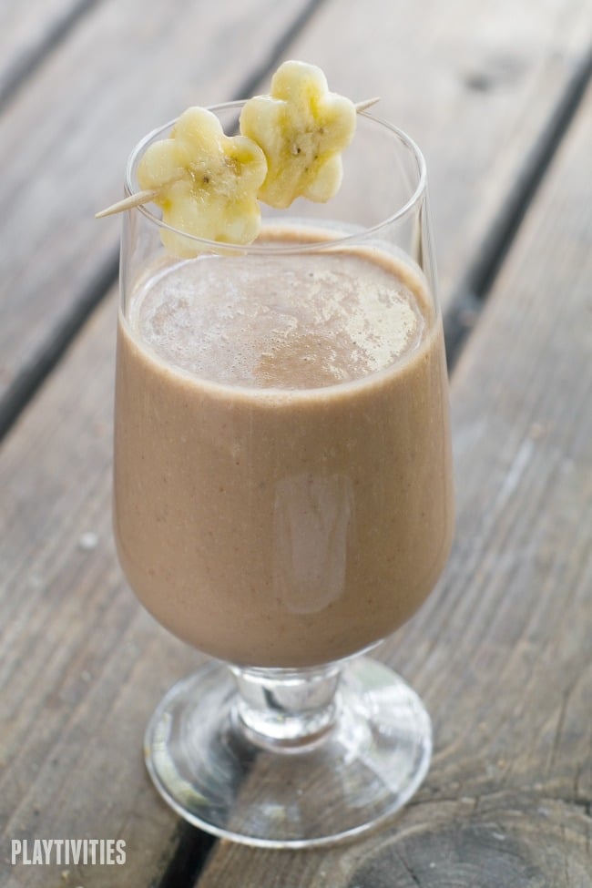 Peanut butter smoothie in a tall glass with sliced banana on a table.
