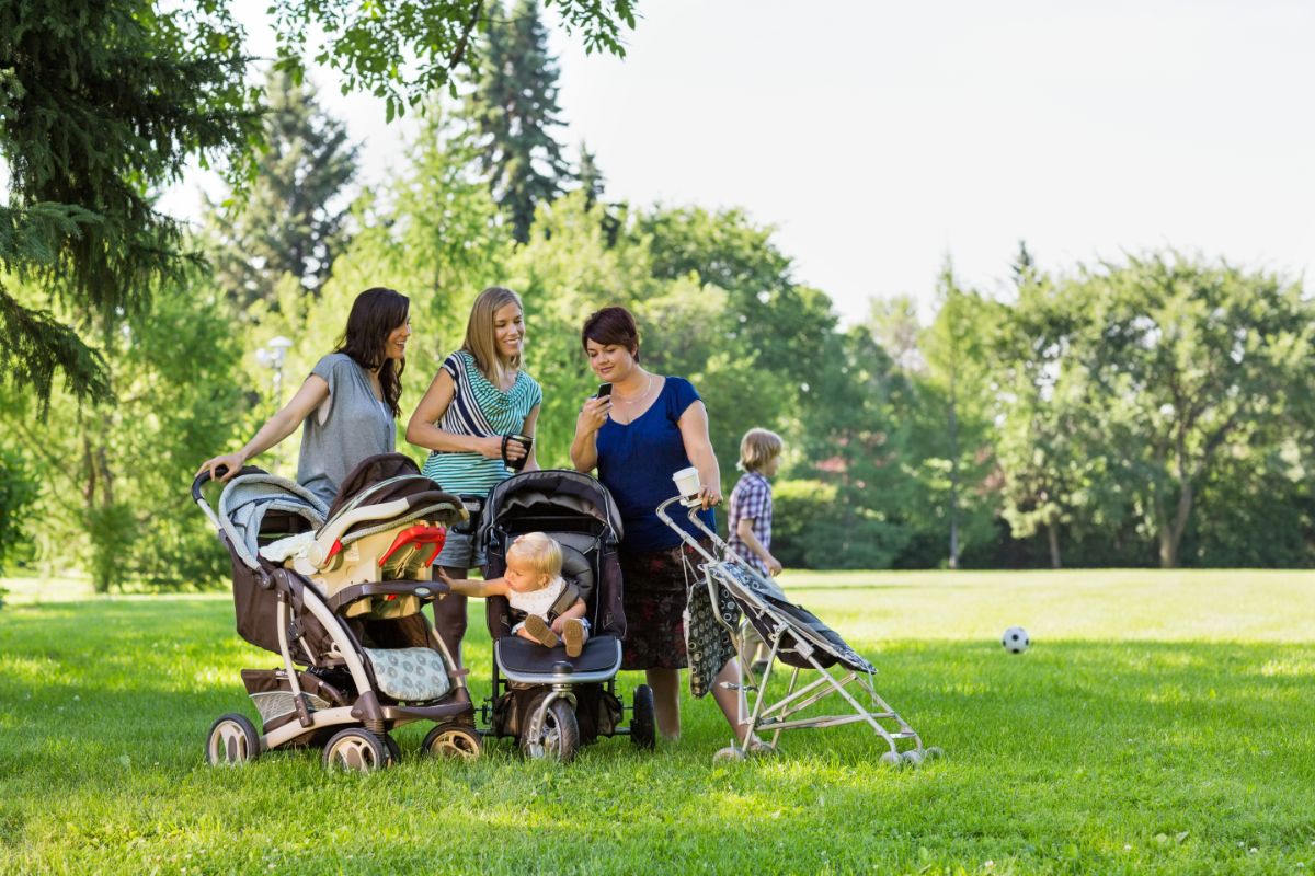3 young moms with baby strollers talking to each other in a park.