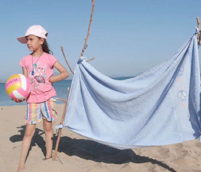 Young girl holding a ball on a beach next to diy net.