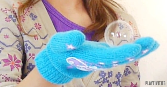 Young girl with a glove holding a bubble.