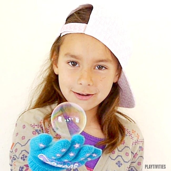 Young girl wih a glove bouncing a bubble.