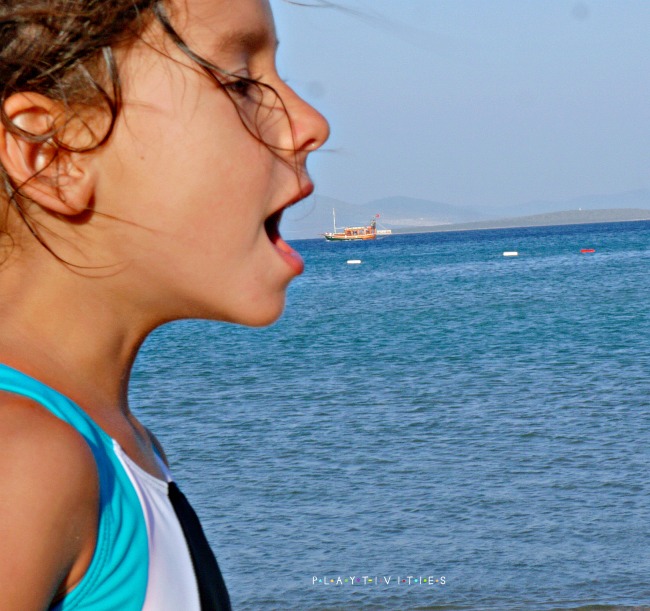 Little girl with open mouth near a sea with a boat.