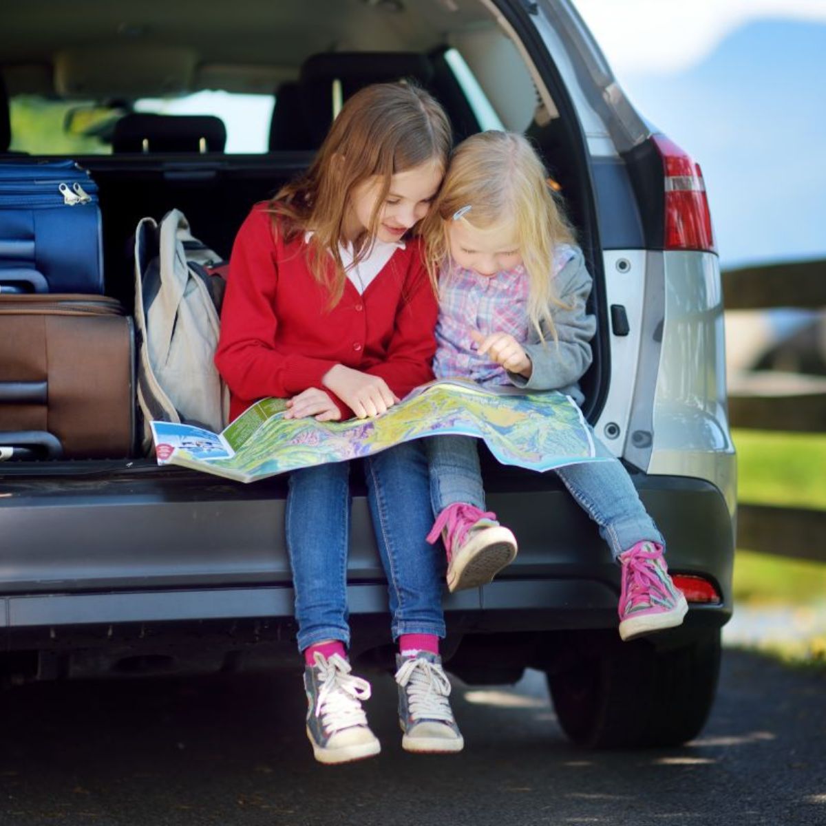 Two kids sitting at car trunk and reading a map.