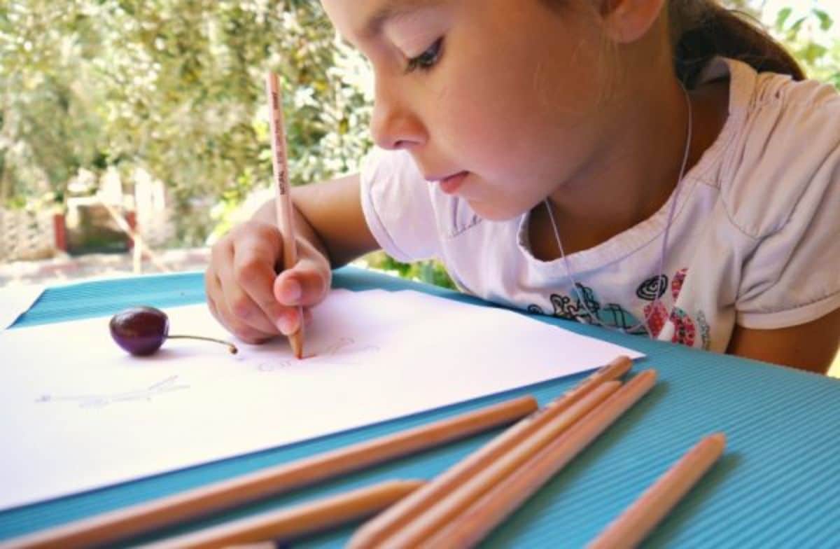 Young girl drawing on a paper sheet with colorful pencils.