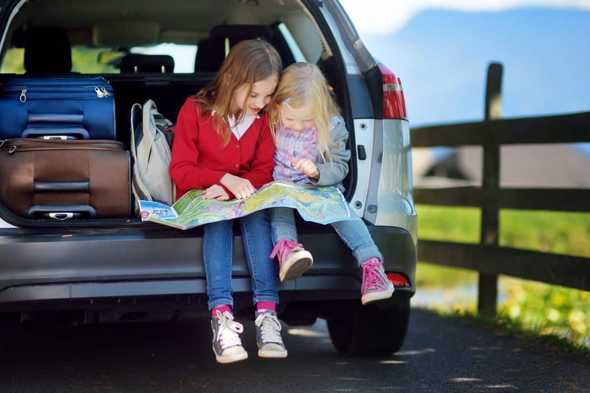 Two kids sitting at a car trunk and reading a map.