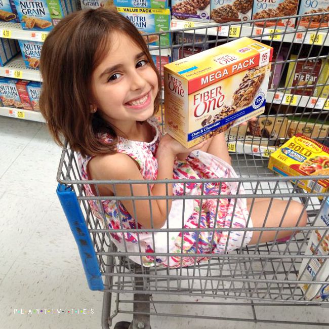 Young girl sitting in a shopping cart and holding a package of fiber dessert.