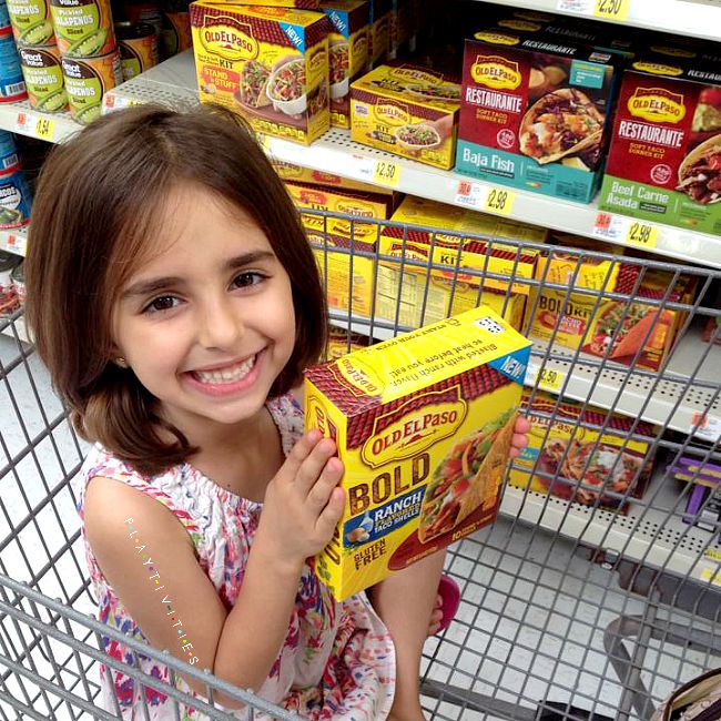 Smiling young girl sitting in a shopping cart and holding a taco package.