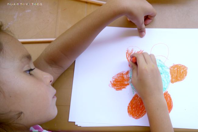 Kid drawing on a paper sheet with crayons.