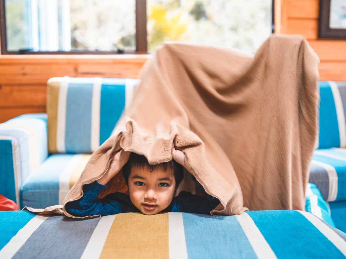 Young boy hiding under blanket playing hide and seek game.