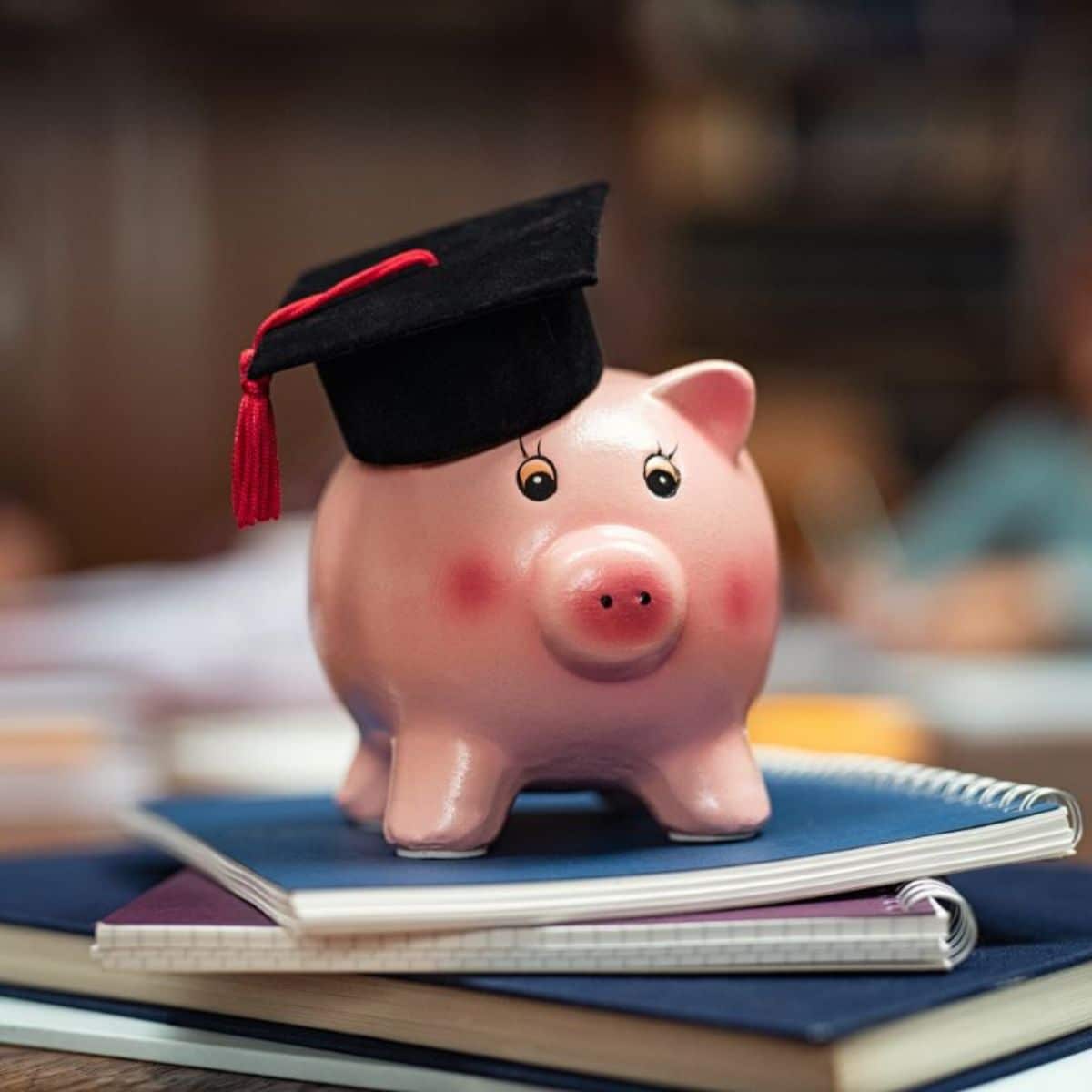 Piggy bank with tiny school hat sitting on a pile of books.