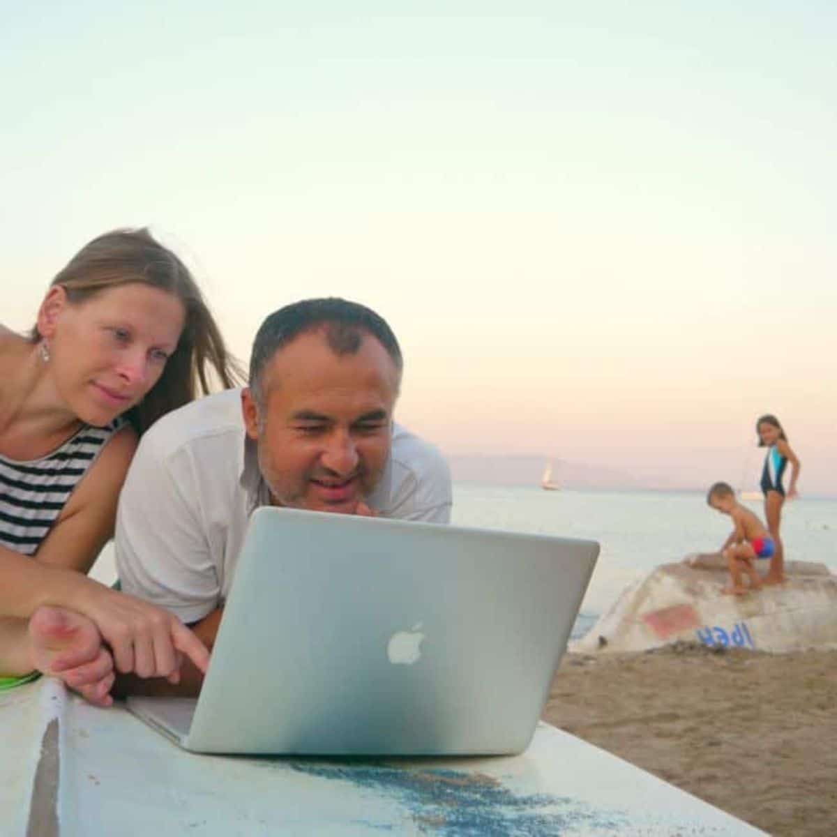 Parents working on laptop from a beach.