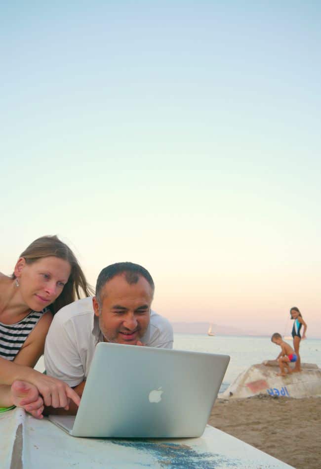 Parents working from a beach on a laptop.