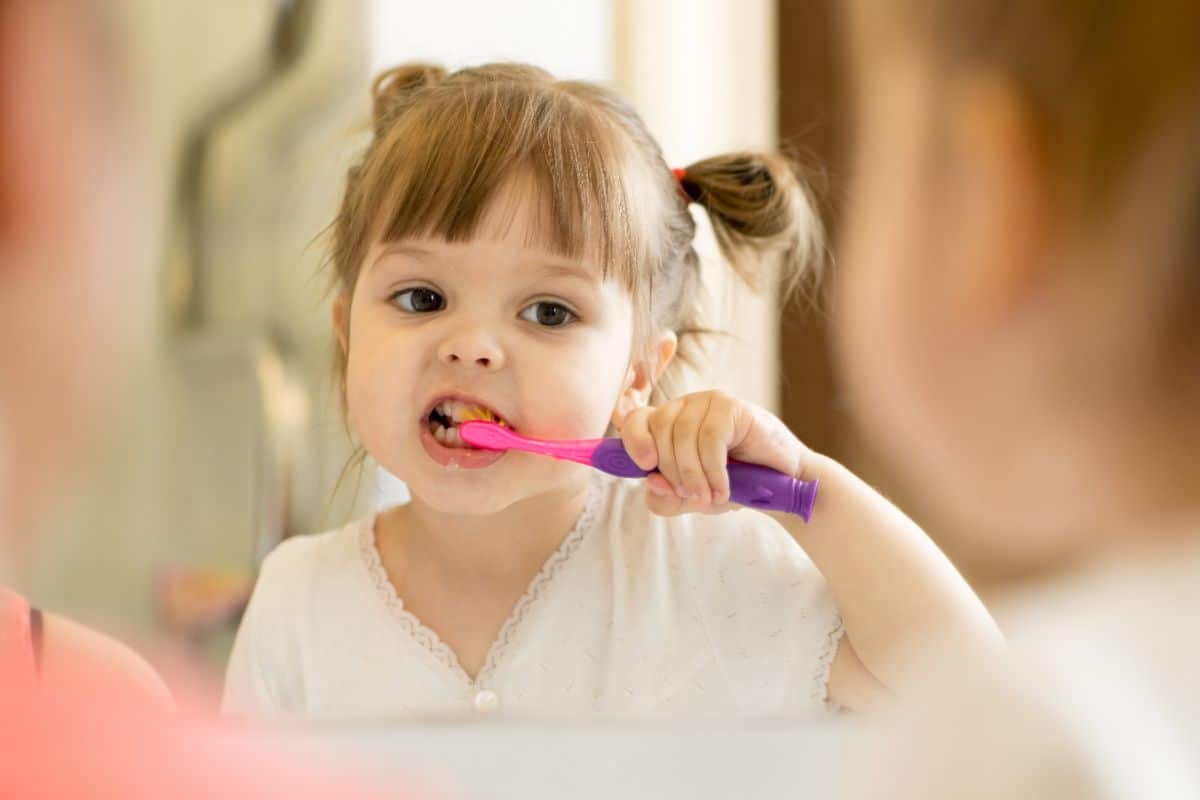 Young girl brushing teeth infront of mirror.