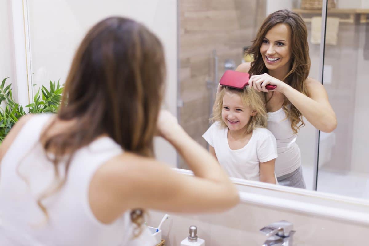 Young mother brushing daughter hair infron ot mirror.