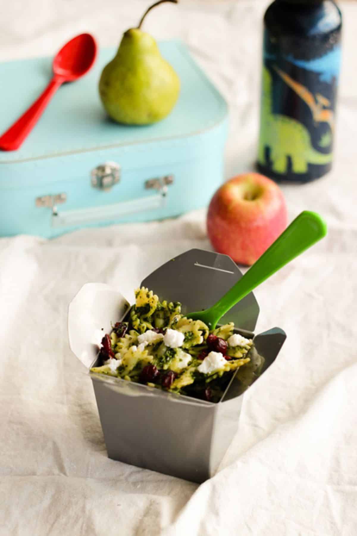 Pasta salad box with a green plastic fork on a table.