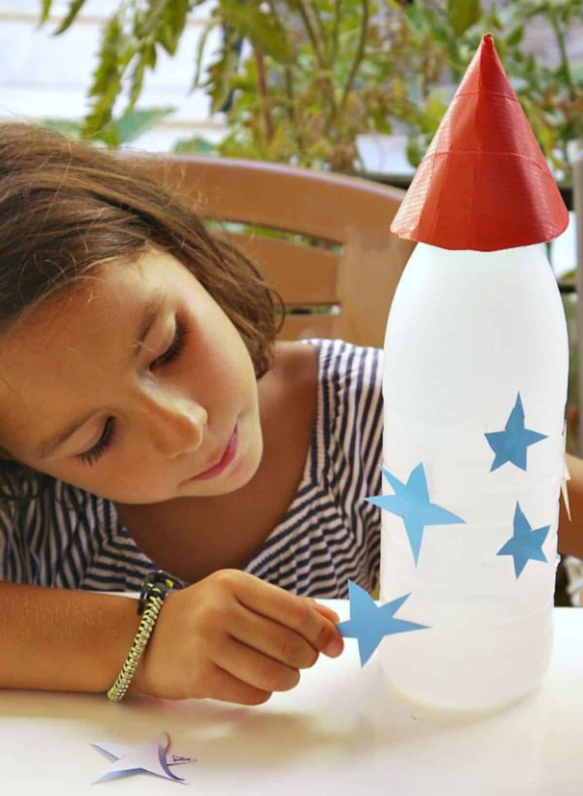 Young girl putting paper starts on a rocket pencil holder.