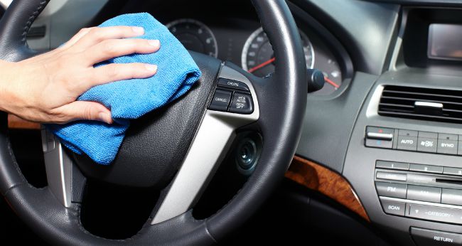 Hand cleaning a car volant with a blue wipe.