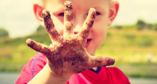 Young boy showing his dirty hand from a sand.