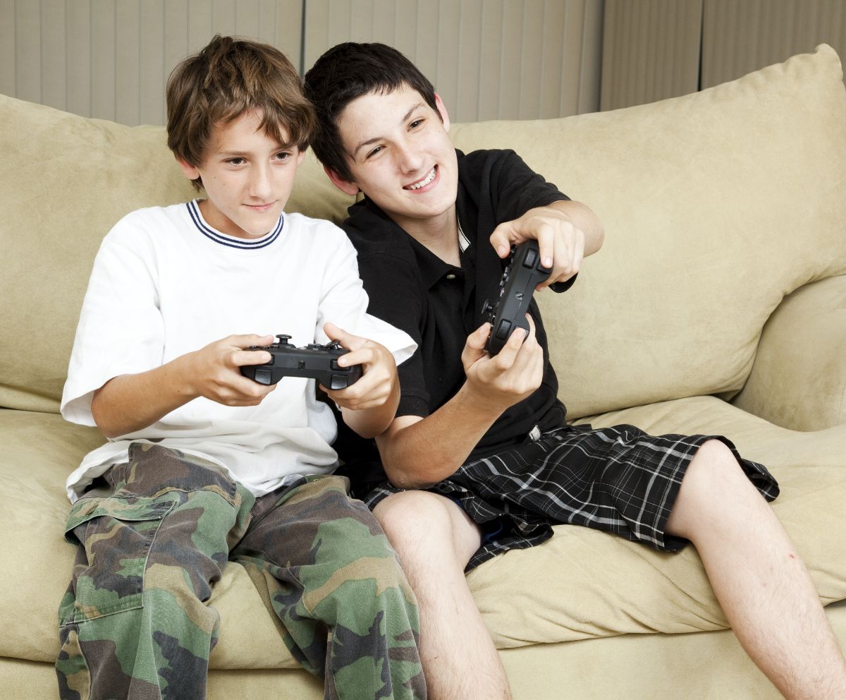 Two boys sitting on a couch and playing video game.
