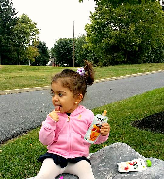 Young girl eating a snack outdoor while sitting on a rock.