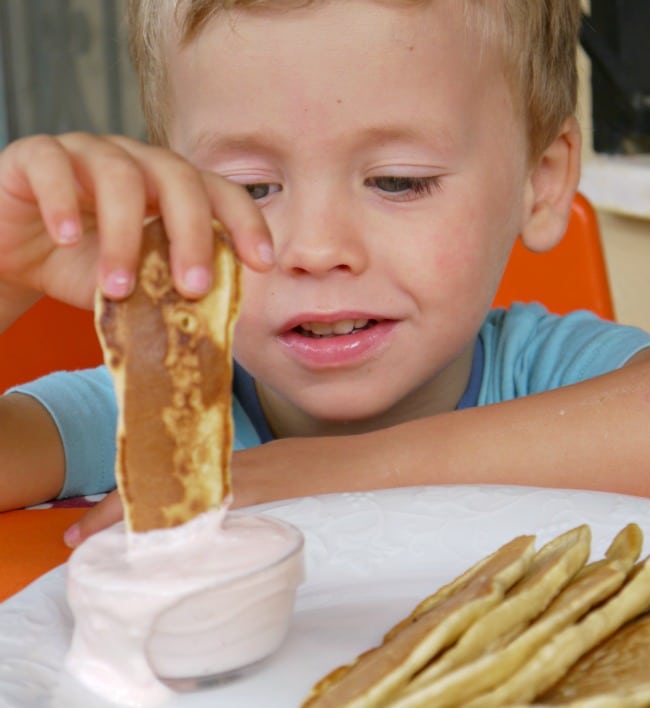 YOung boy dipping pancake dippers in a bowl of yogurt on a plate.
