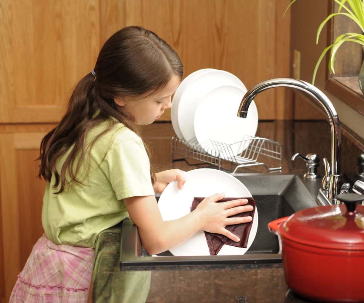 Young girl beind the sink washing dishes.