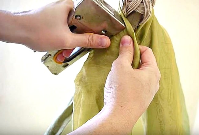 Hands stapling a fabric on a teepee tied sticks.