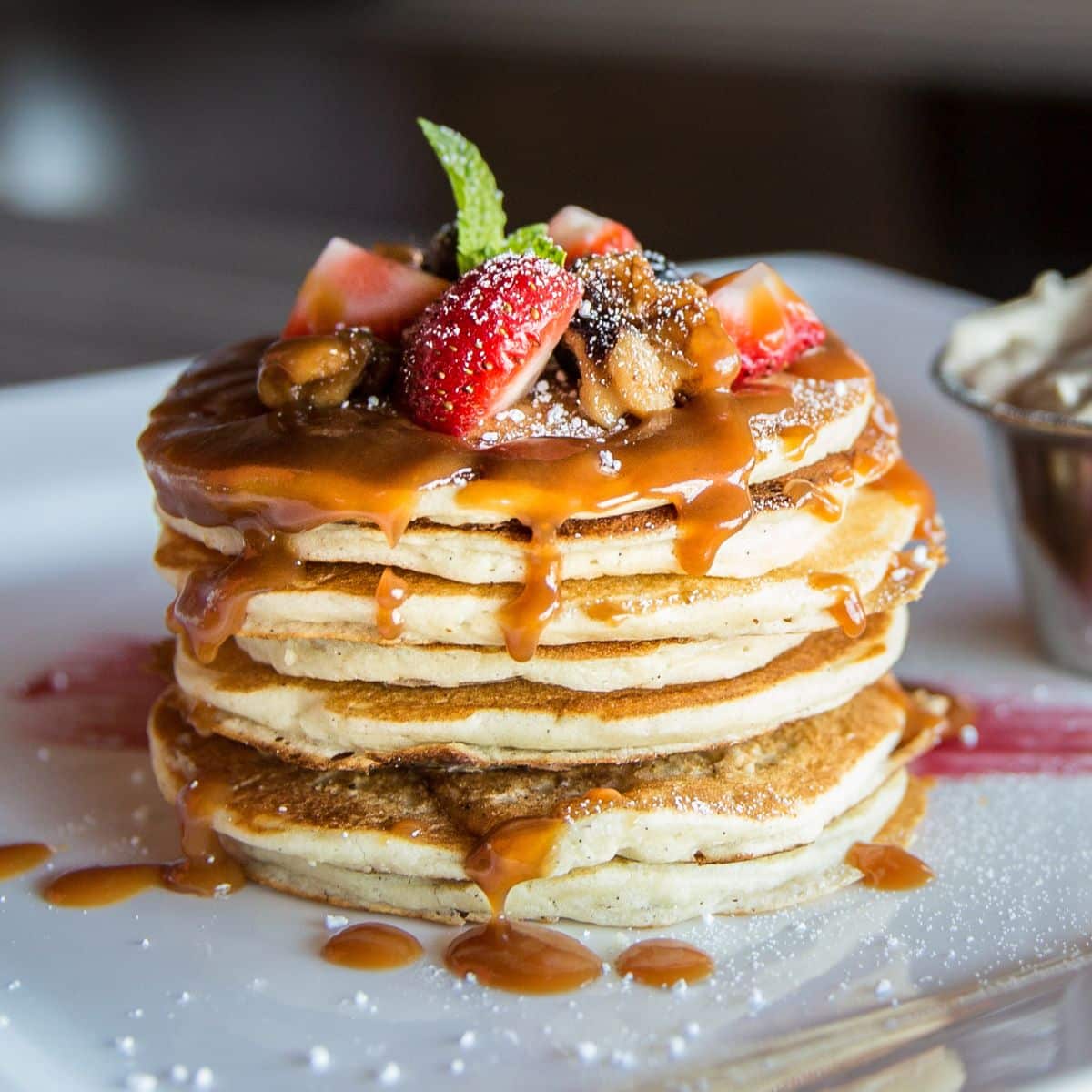 Pile of yummy pancakes with sliced fruits and drizzled frosting on the top on a plate.