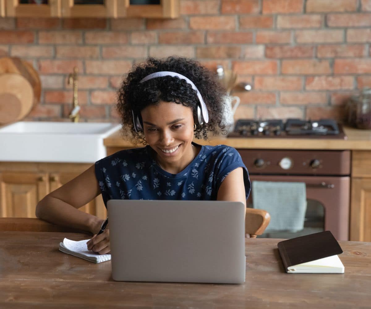 Young black woman with headphone sitting behind the table and looking at laptop.