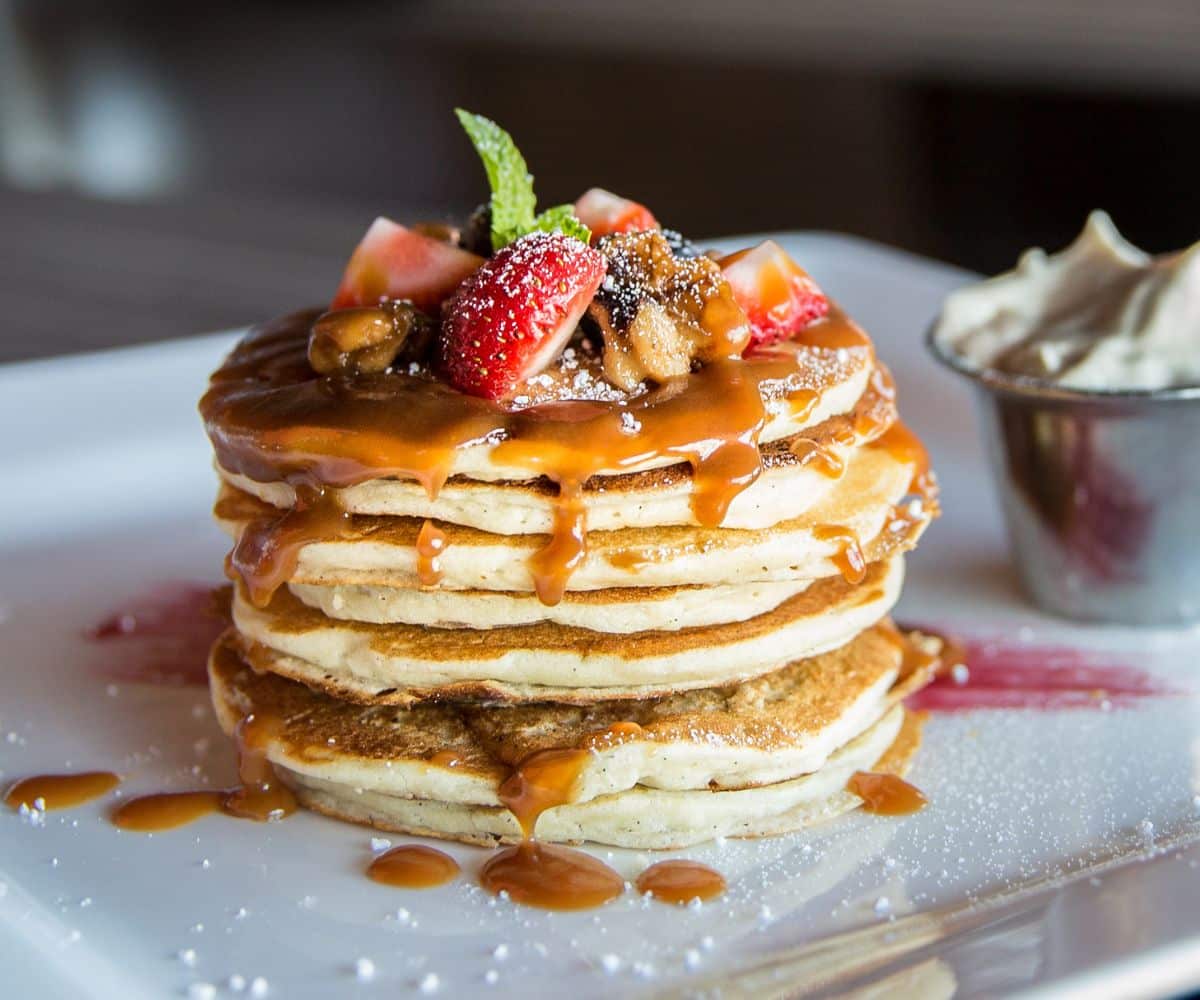 Pile of yummy looking pancakes on a tray with sliced fruits on the top.