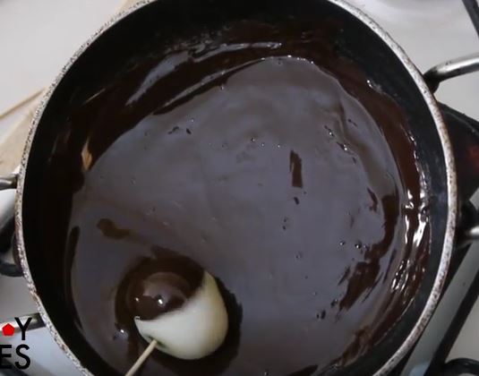 DIpping raw onion in a pan with melted chocolate.