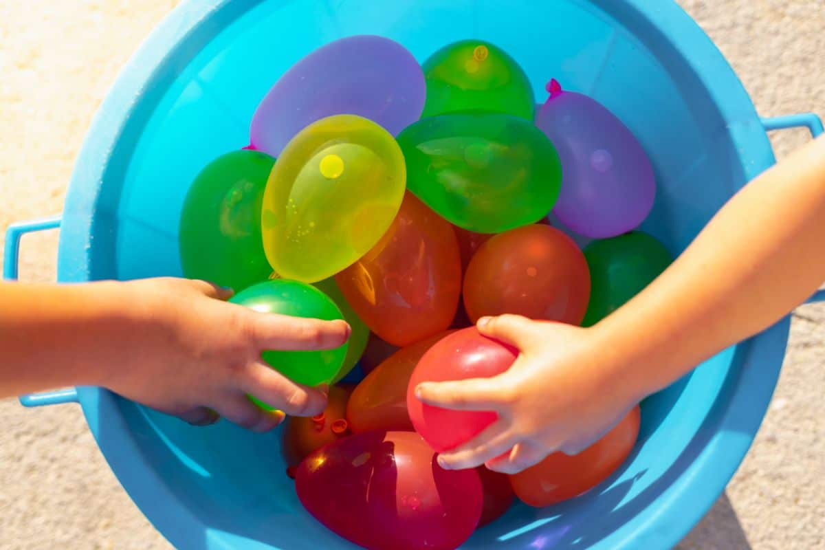 Kid hands pickung water balloons from a blue bowl.