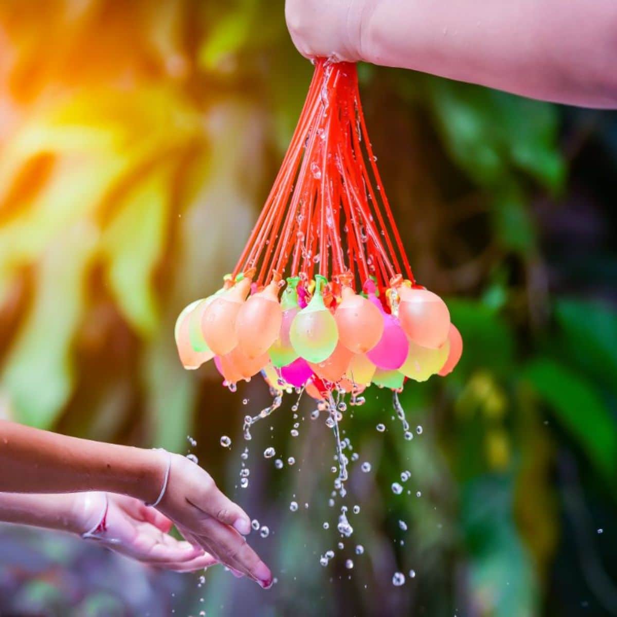 Hand holding bunch of water balloons over kid hands,